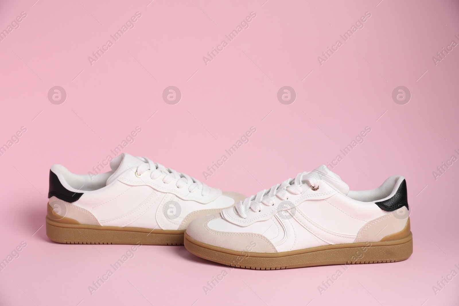 Photo of Pair of stylish sneakers on pale pink background. Casual shoes