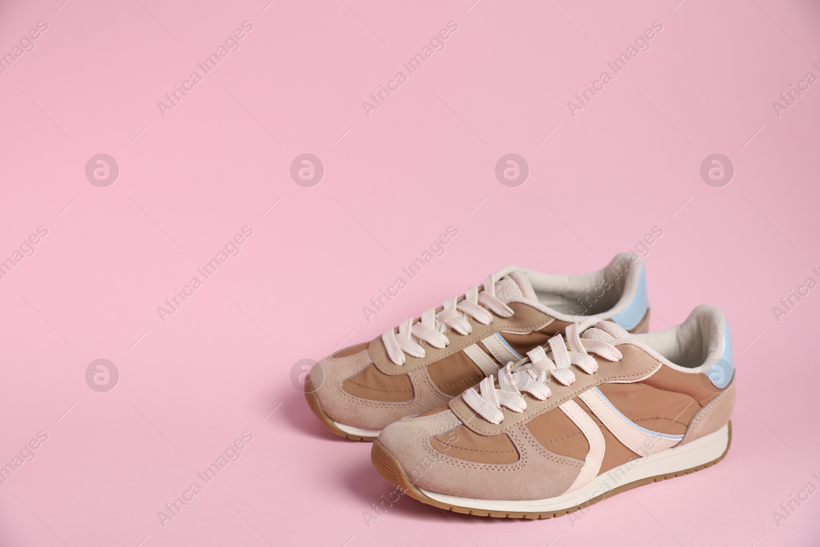 Photo of Pair of stylish sneakers on pale pink background, space for text. Casual shoes