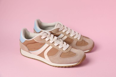 Photo of Pair of stylish sneakers on pale pink background. Casual shoes