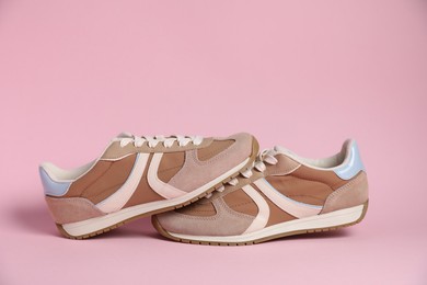 Photo of Pair of stylish sneakers on pale pink background. Casual shoes