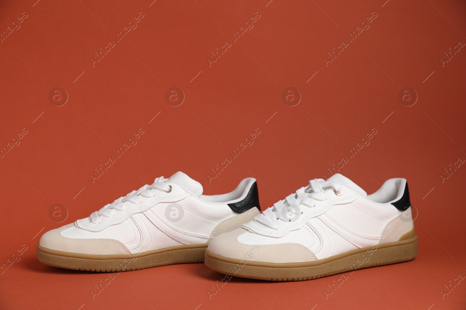 Photo of Pair of stylish sneakers on red-brown background. Casual shoes