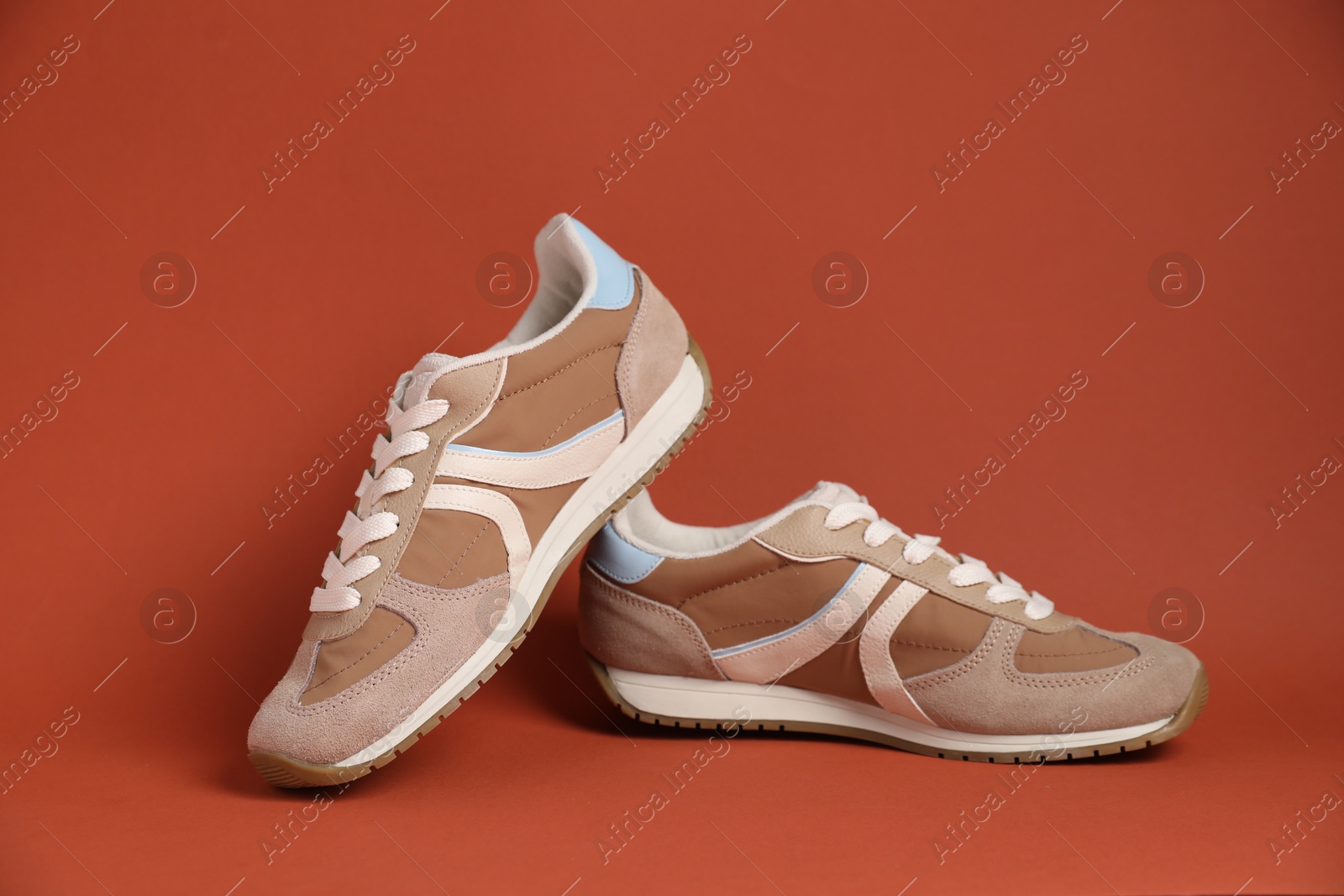 Photo of Pair of stylish sneakers on red-brown background. Casual shoes