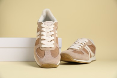 Photo of Pair of stylish sneakers and box on beige background. Casual shoes