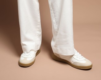 Photo of Woman wearing stylish sneakers on light brown background, closeup