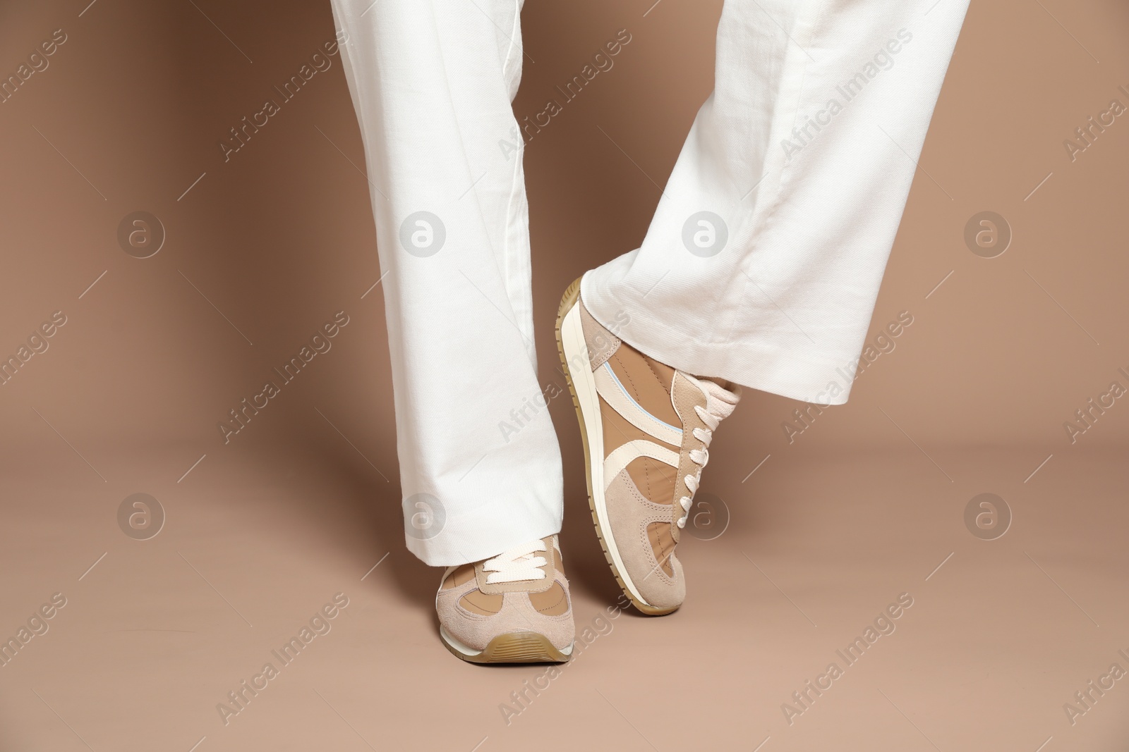Woman wearing stylish sneakers on light brown background, closeup Photo of Woman wearing stylish sneakers on light brown background, closeup