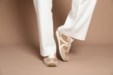 Photo of Woman wearing stylish sneakers on light brown background, closeup