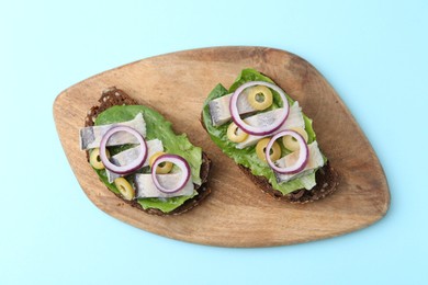 Photo of Tasty sandwiches with herring, onions and olives on light blue background, top view