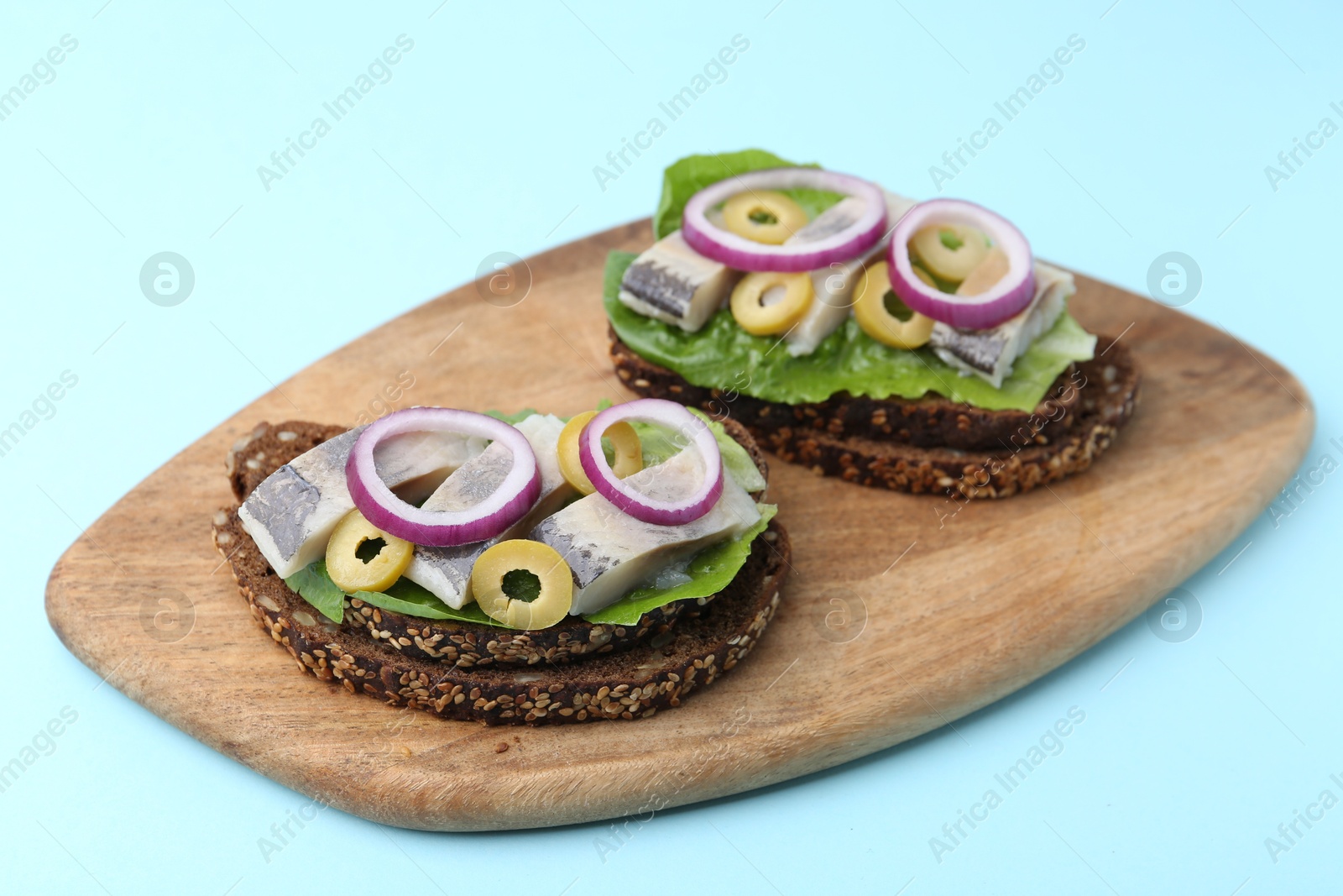 Photo of Tasty sandwiches with herring, onions and olives on light blue background, closeup