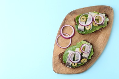 Photo of Tasty sandwiches with herring, onions and olives on light blue background, top view. Space for text