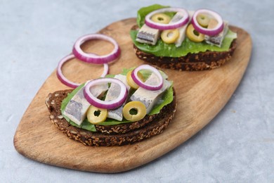 Photo of Tasty sandwiches with herring, onions and olives on light grey table, closeup