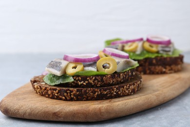 Tasty sandwiches with herring, onions and olives on light grey table, closeup