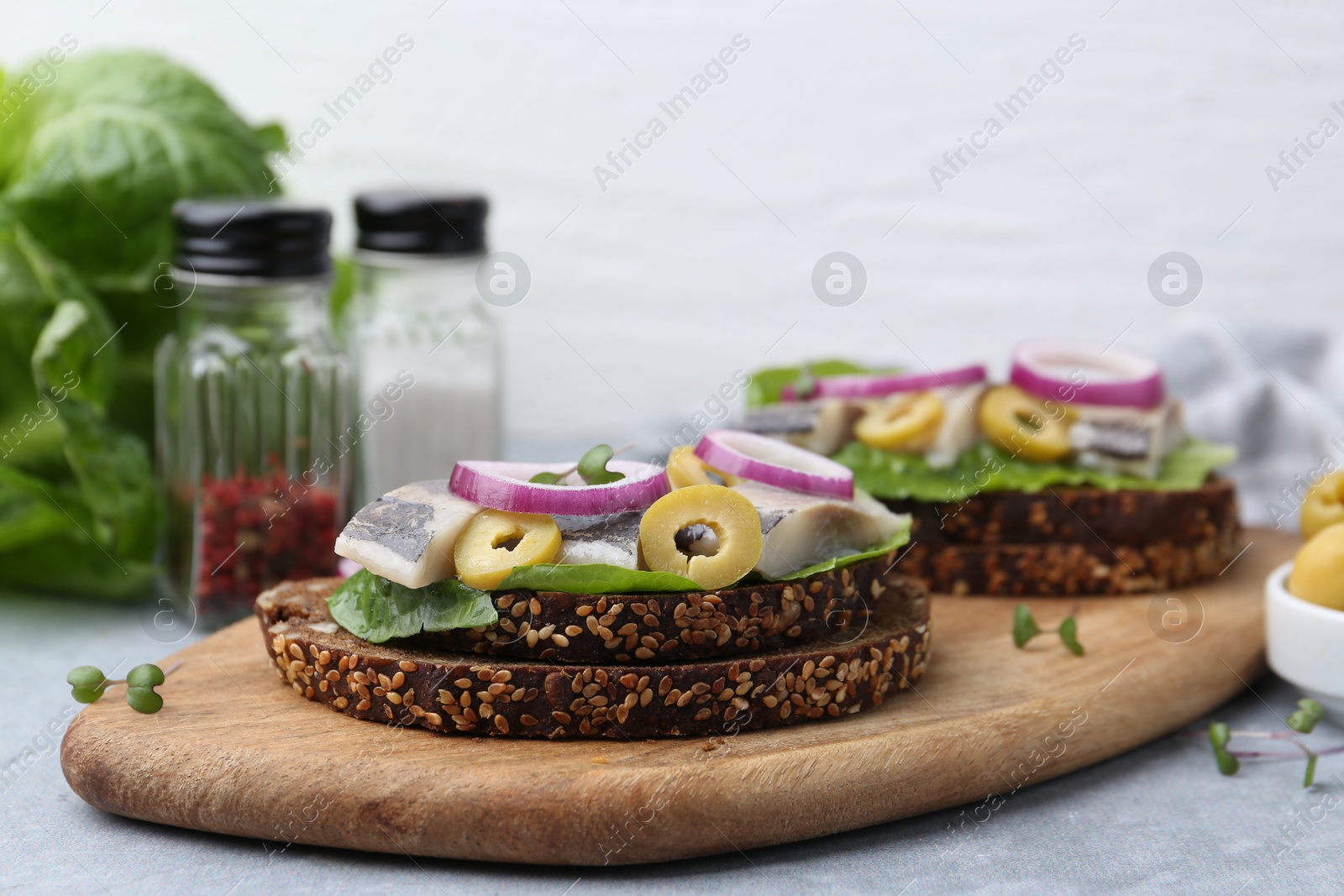 Photo of Tasty sandwiches with herring, onions and olives on light grey table, closeup