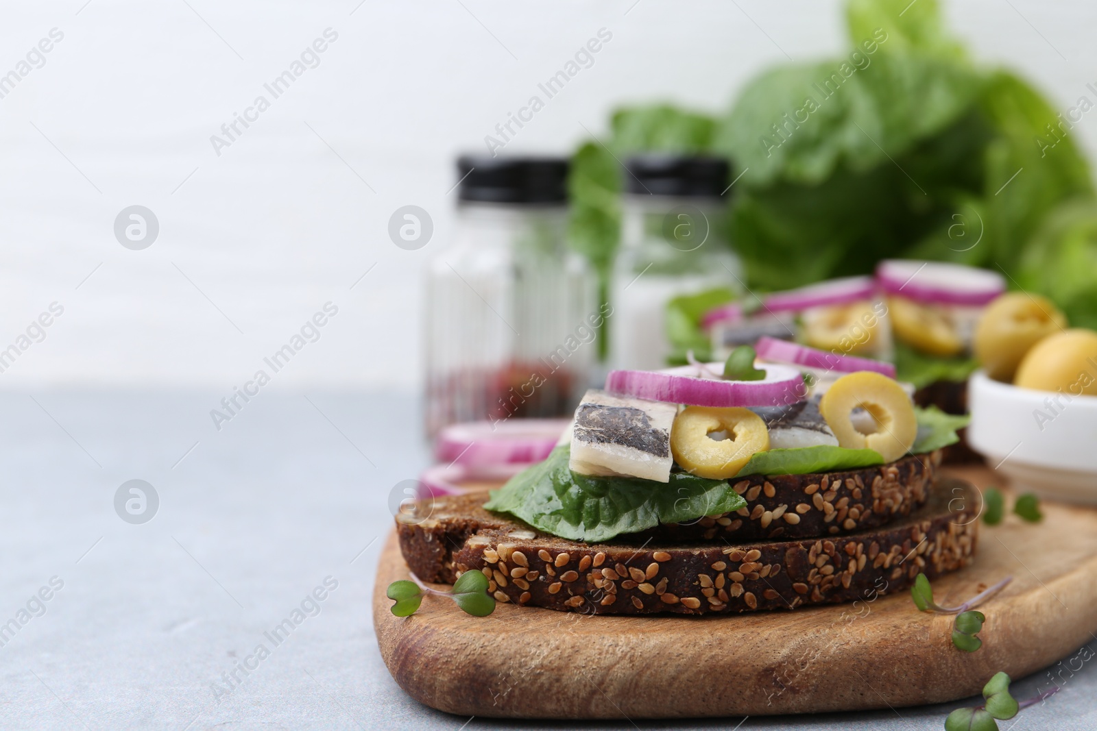 Photo of Tasty sandwich with herring, onion and olives on light grey table, closeup. Space for text