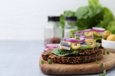 Tasty sandwich with herring, onion and olives on light grey table, closeup. Space for text