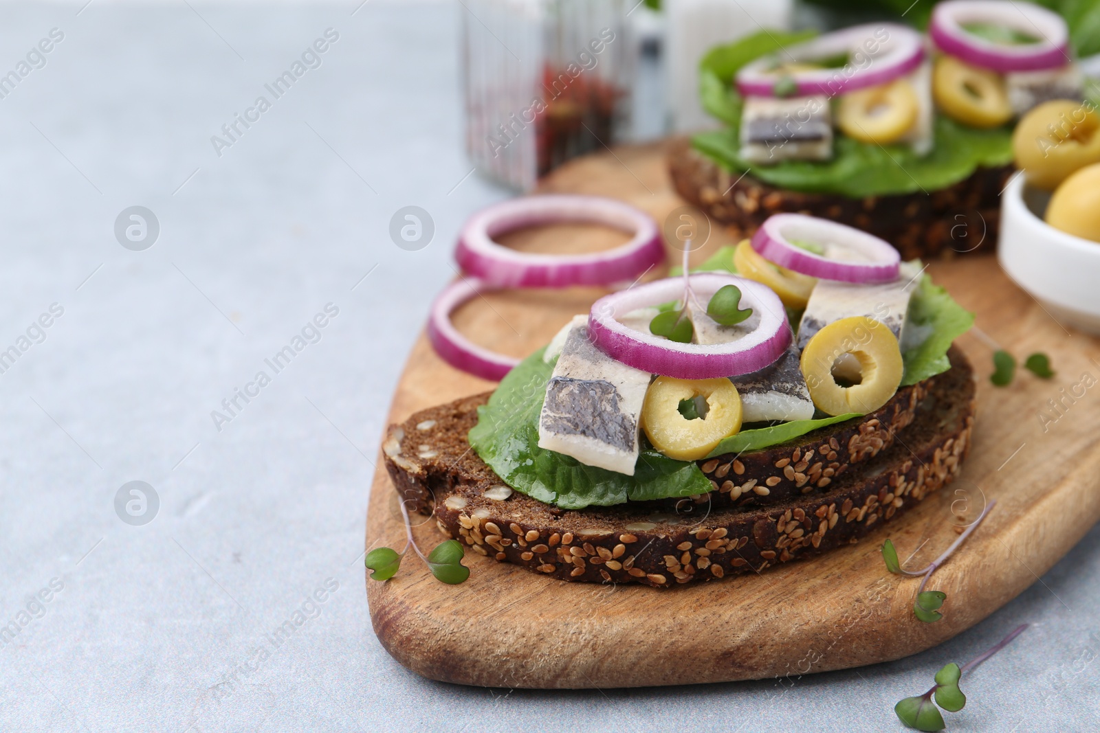 Photo of Tasty sandwiches with herring, onions and olives on light grey table, closeup. Space for text