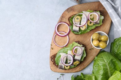 Photo of Tasty sandwiches with herring, onions, lettuce and olives on light grey table, flat lay. Space for text