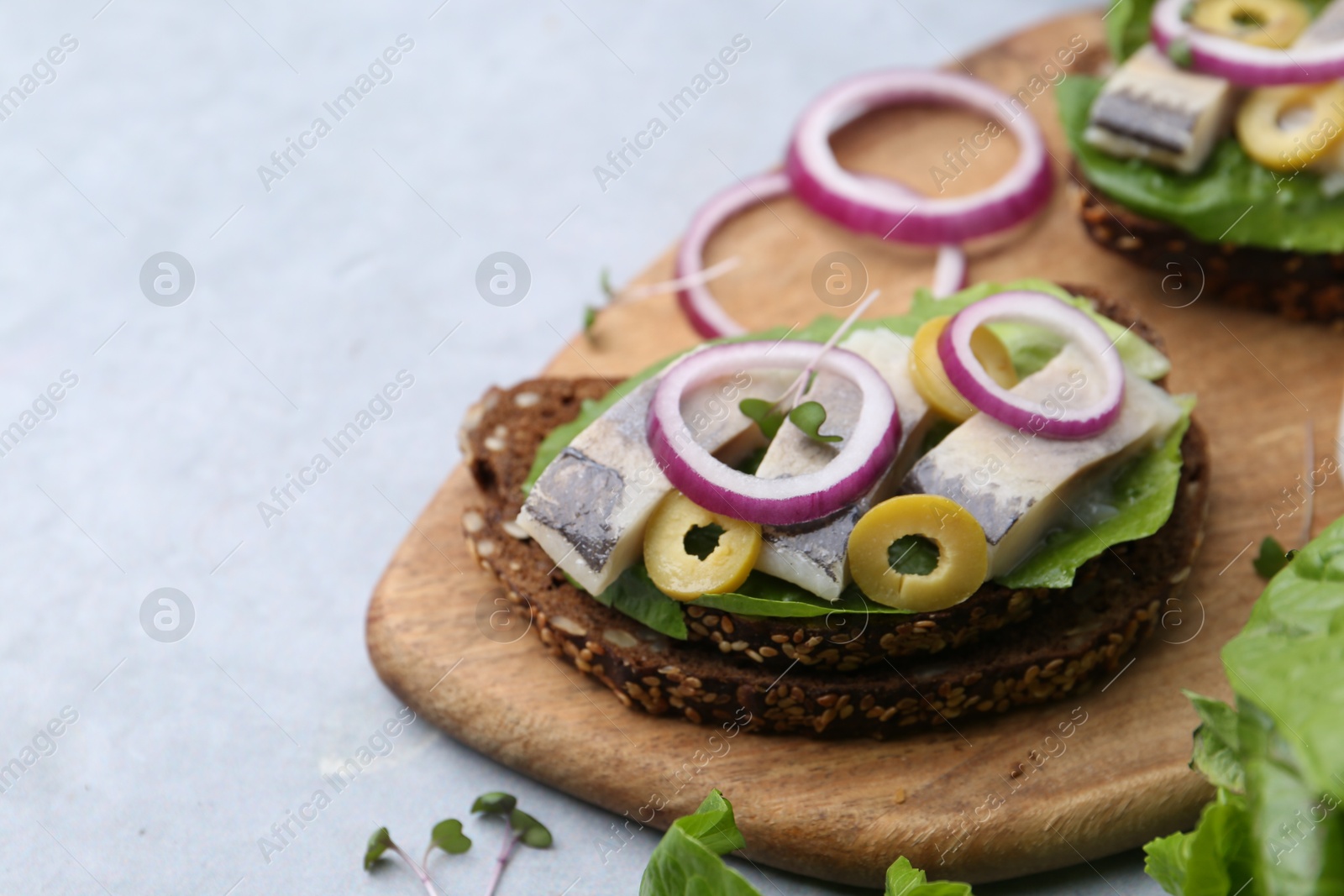 Photo of Tasty sandwich with herring, onion and olives on light grey table, closeup. Space for text