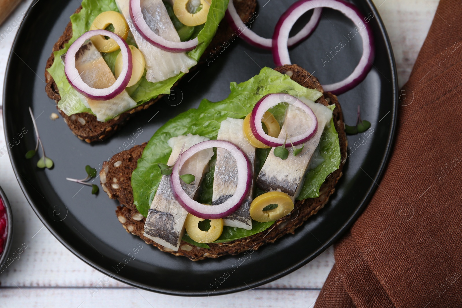 Photo of Tasty sandwiches with herring, onions, lettuce and olives on white wooden table, top view