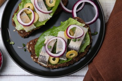 Photo of Tasty sandwiches with herring, onions, lettuce and olives on white wooden table, top view