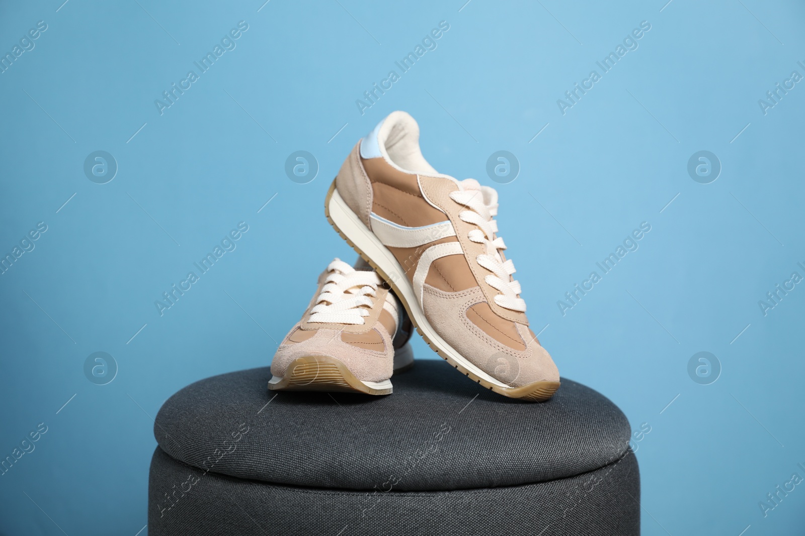 Photo of Pair of stylish sneakers on pouf against light blue background