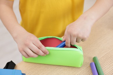 Photo of Boy packing pencil case at wooden table indoors, closeup