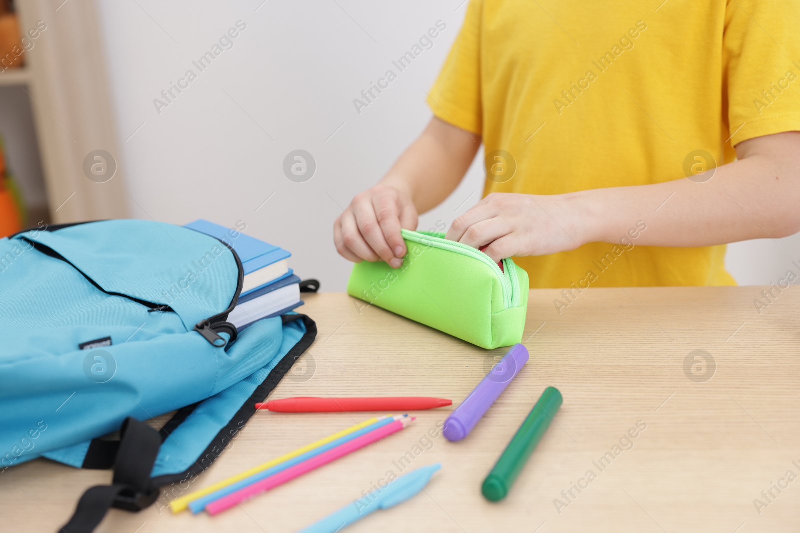 Photo of Boy packing pencil case at wooden table indoors, closeup