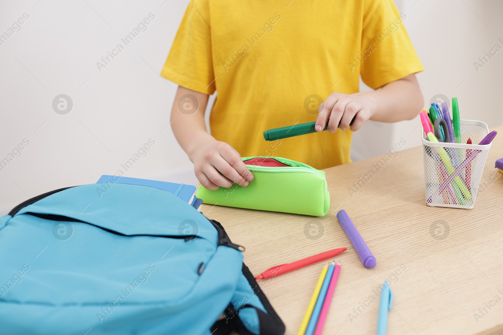 Photo of Boy packing pencil case at wooden table indoors, closeup