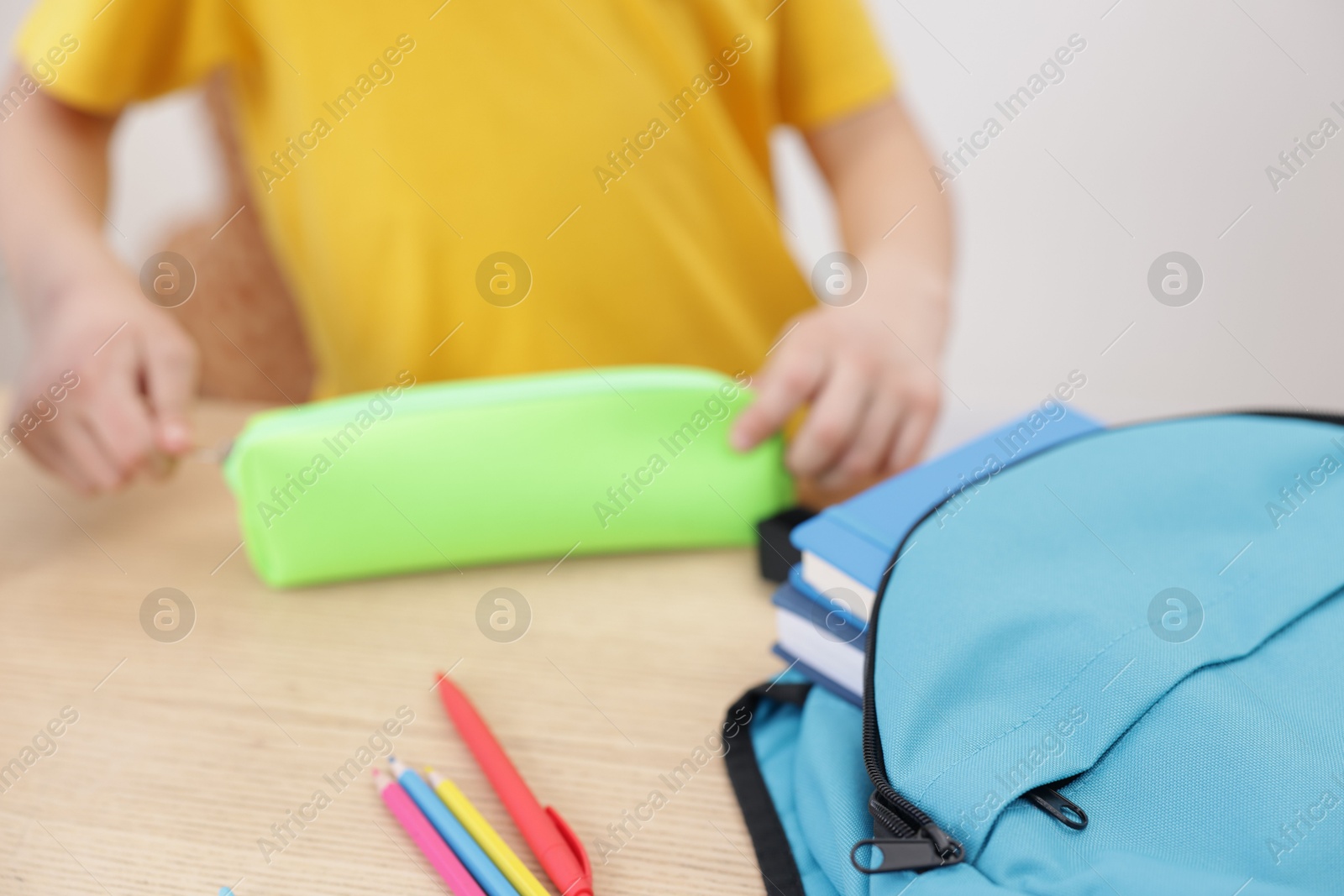 Photo of Boy packing pencil case at wooden table indoors, focus on backpack and stationery