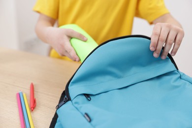 Boy packing backpack for school at wooden table indoors, closeup