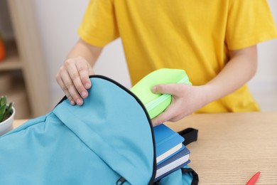 Boy packing backpack for school at wooden table indoors, closeup