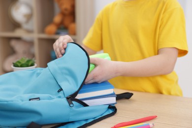 Photo of Boy packing backpack for school at wooden table indoors, closeup