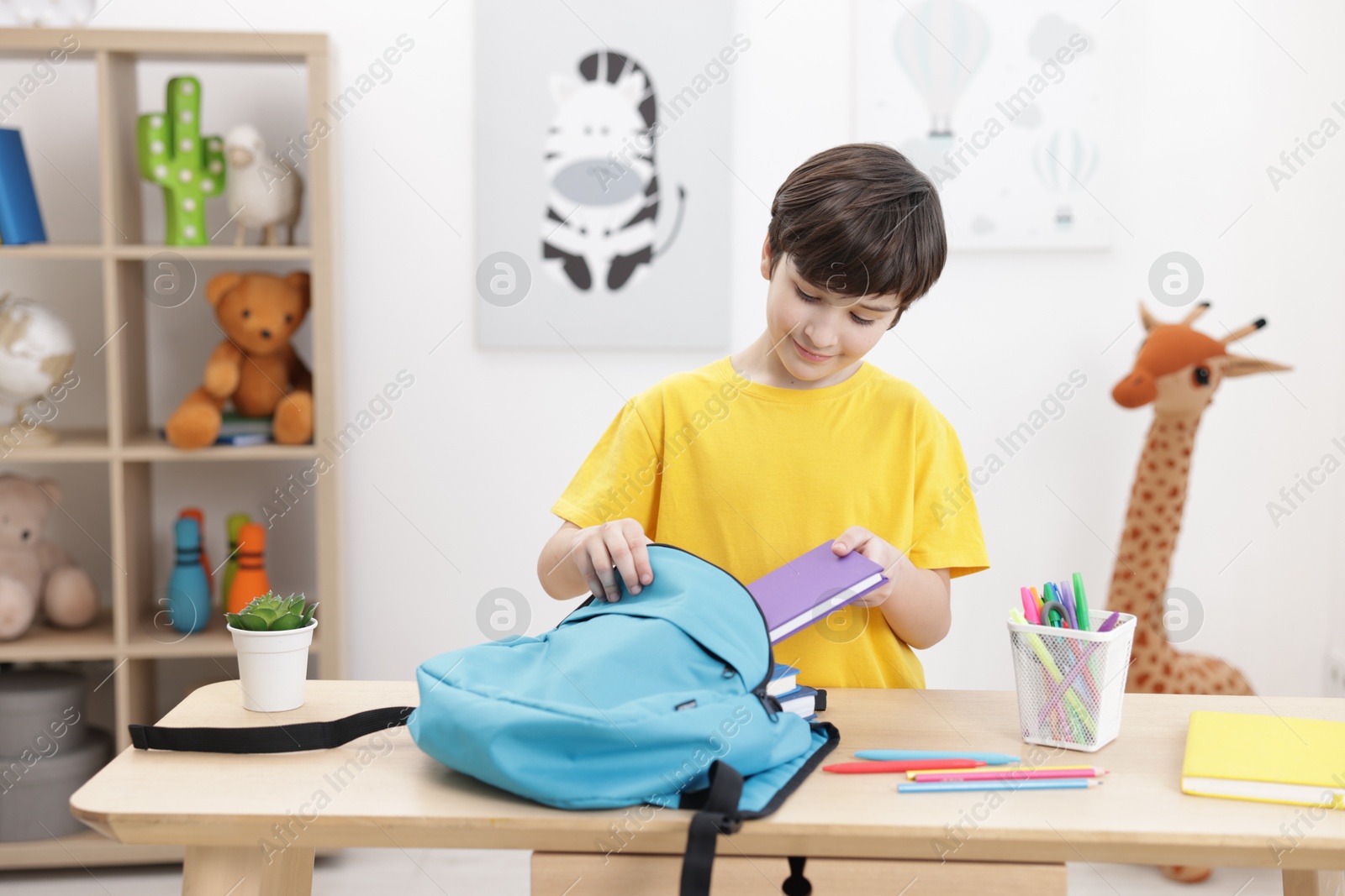 Photo of Boy packing backpack for school at wooden table indoors