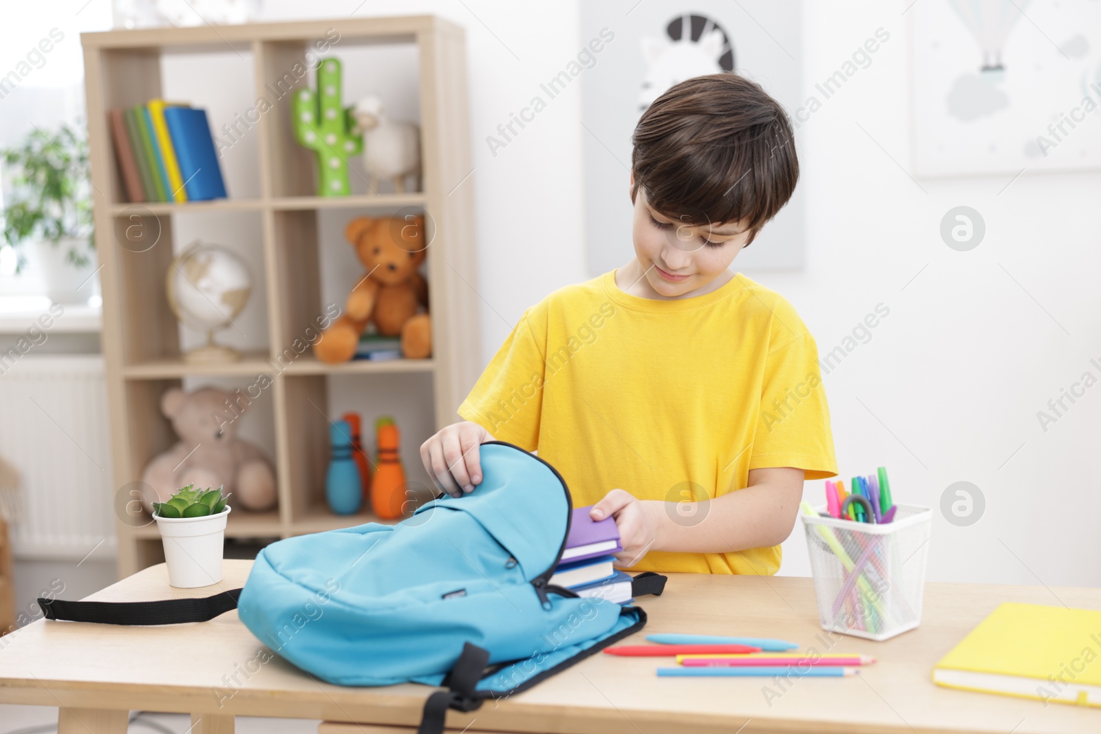 Photo of Boy packing backpack for school at wooden table indoors