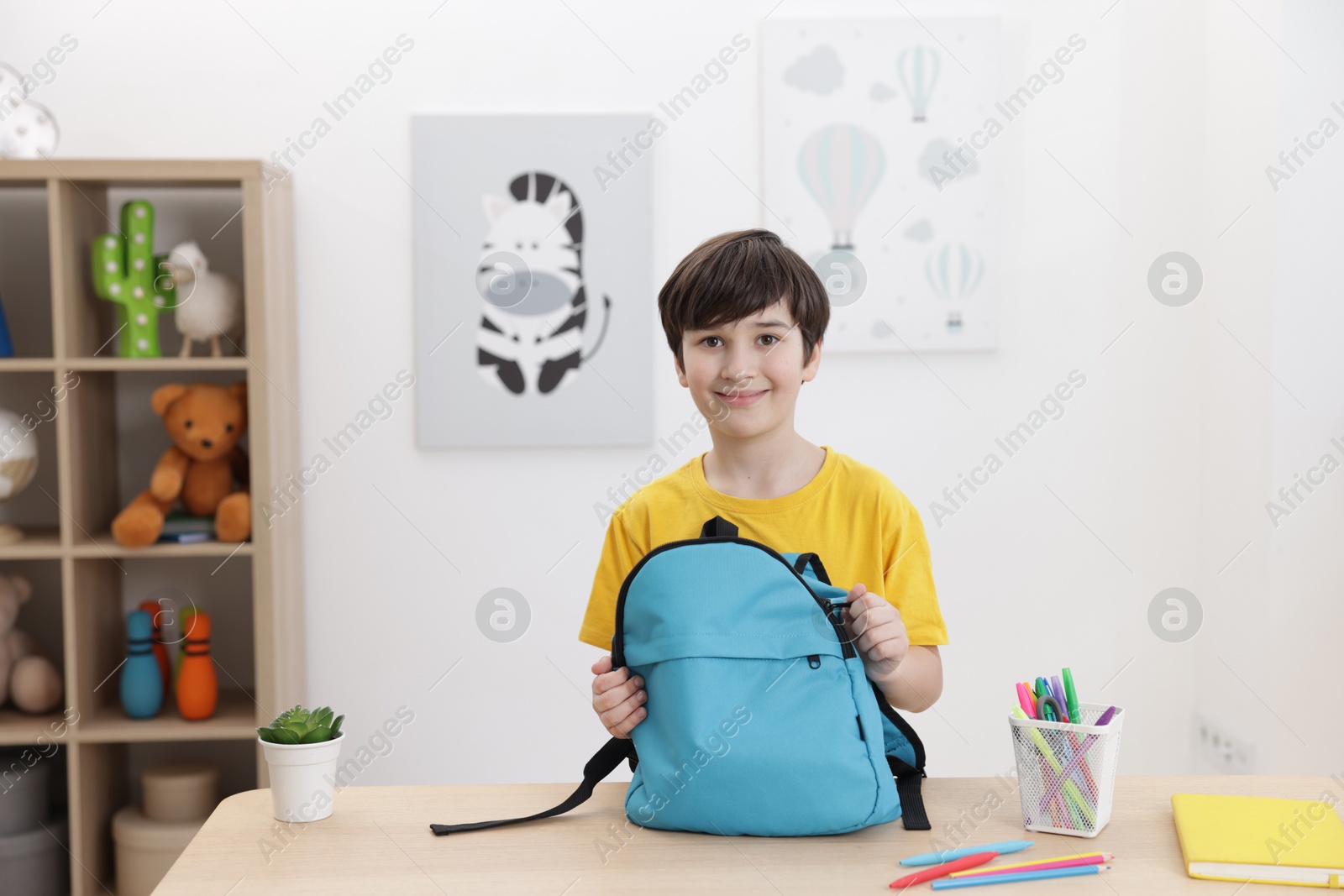 Photo of Boy packing backpack for school at wooden table indoors