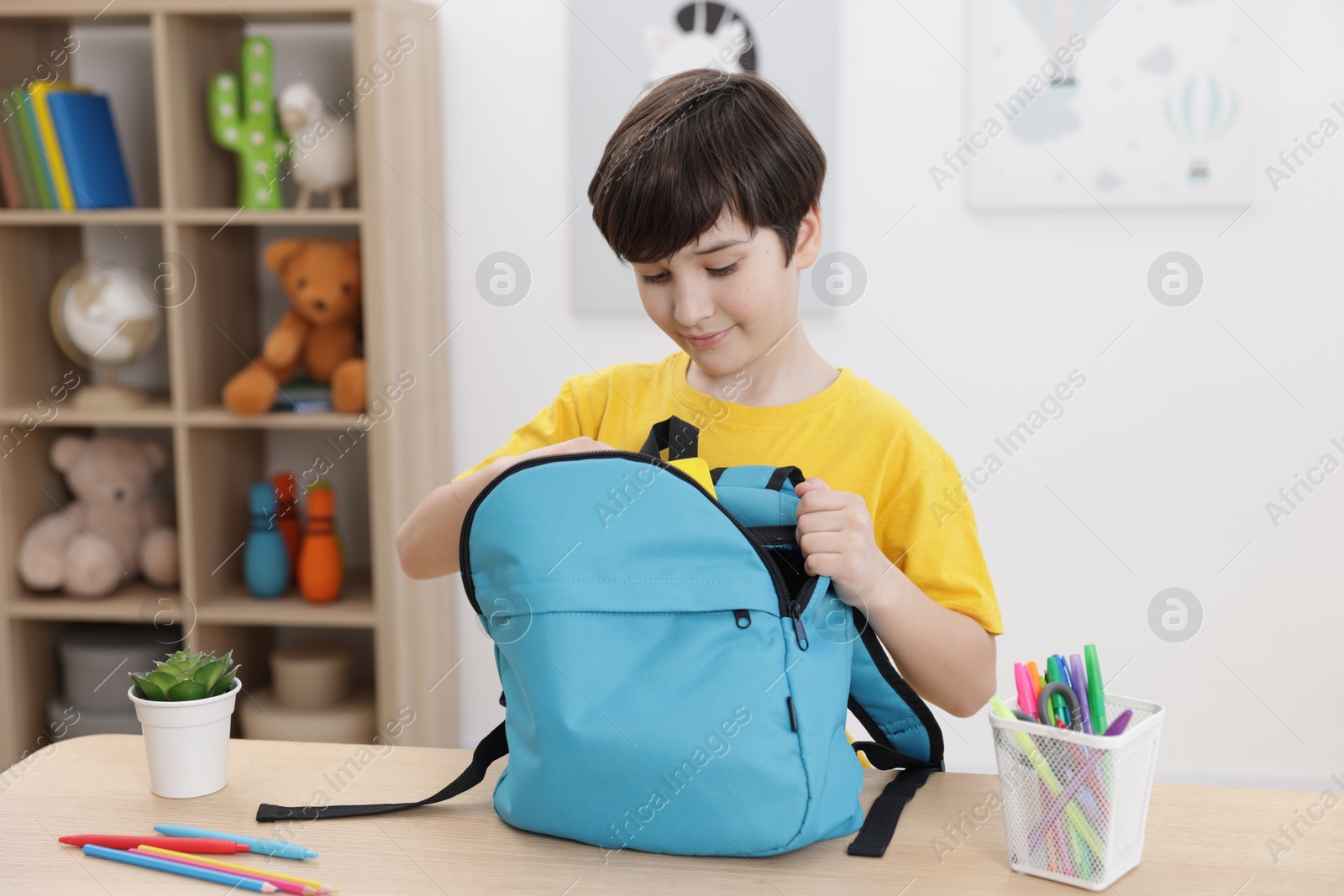 Photo of Boy packing backpack for school at wooden table indoors