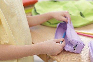 Little girl packing pencil case at wooden table indoors, closeup