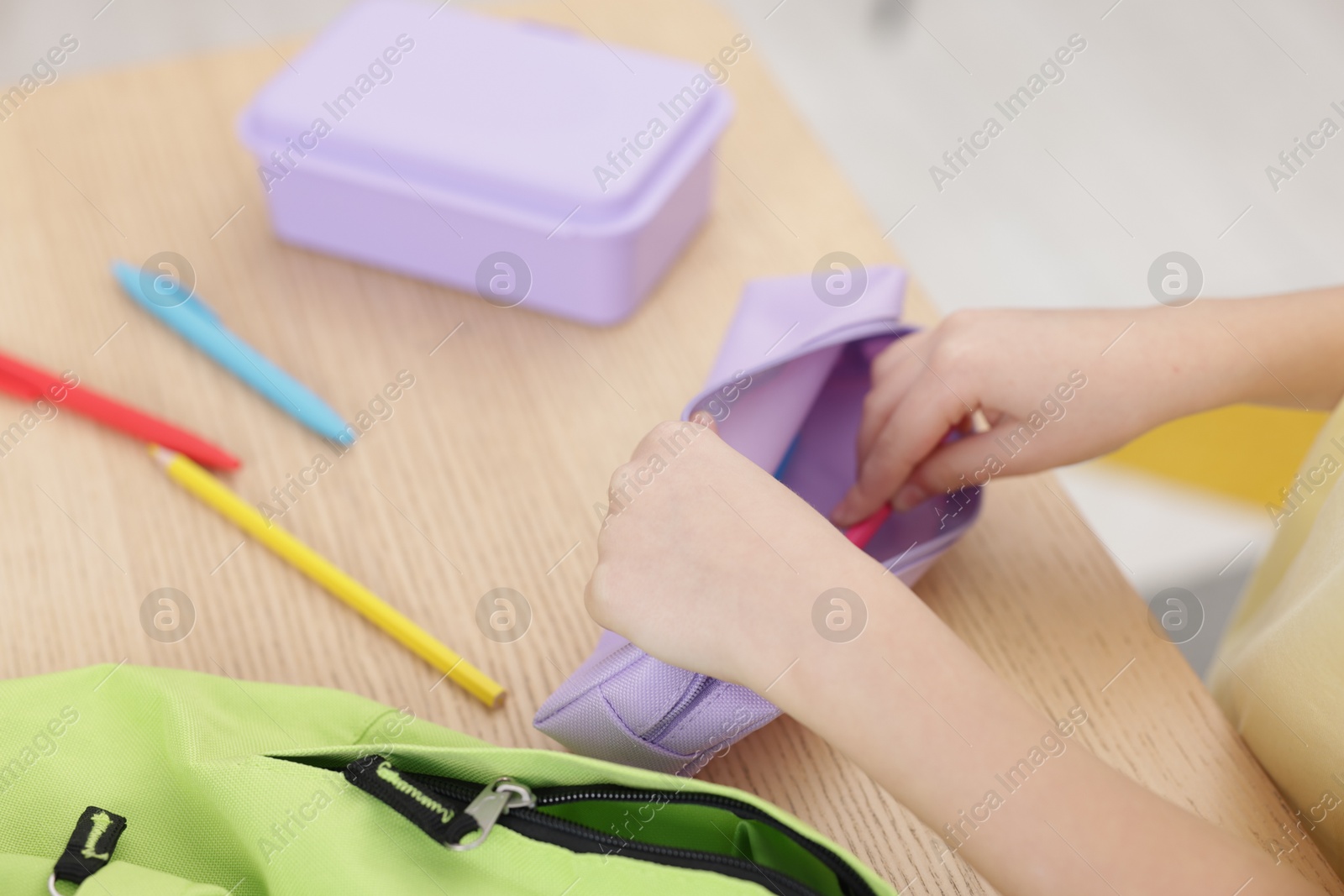 Photo of Little girl packing pencil case at wooden table indoors, closeup