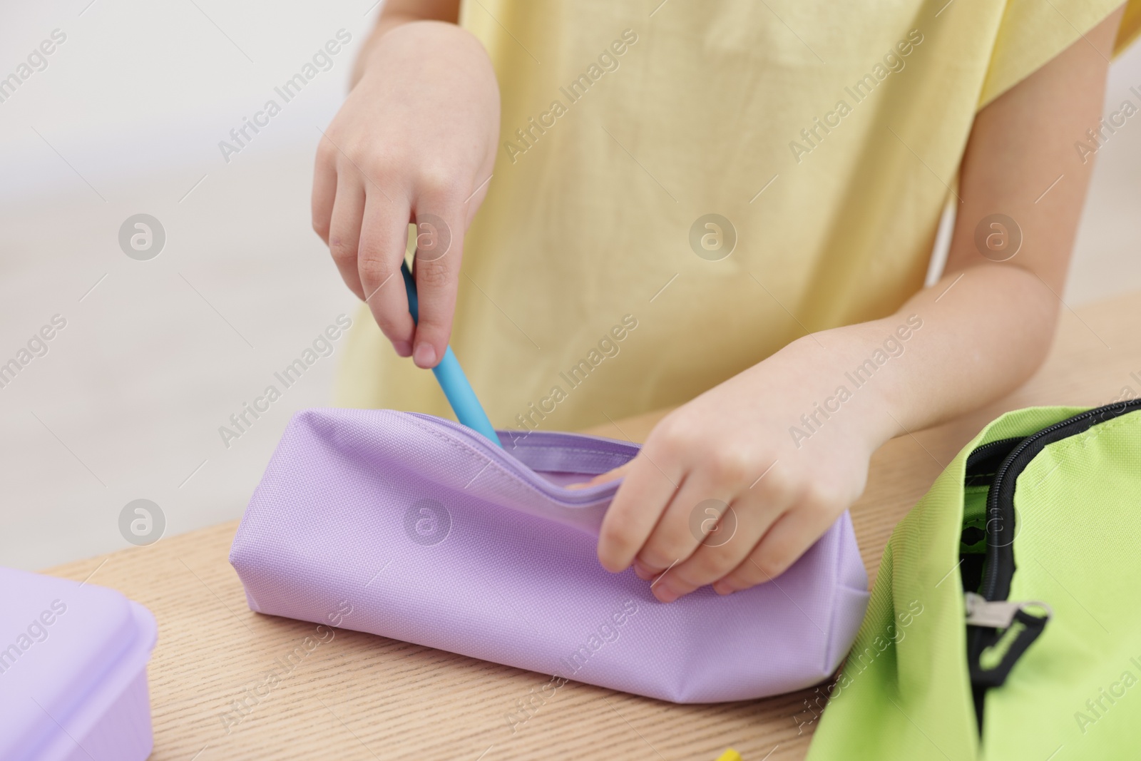 Photo of Little girl packing pencil case at wooden table indoors, closeup