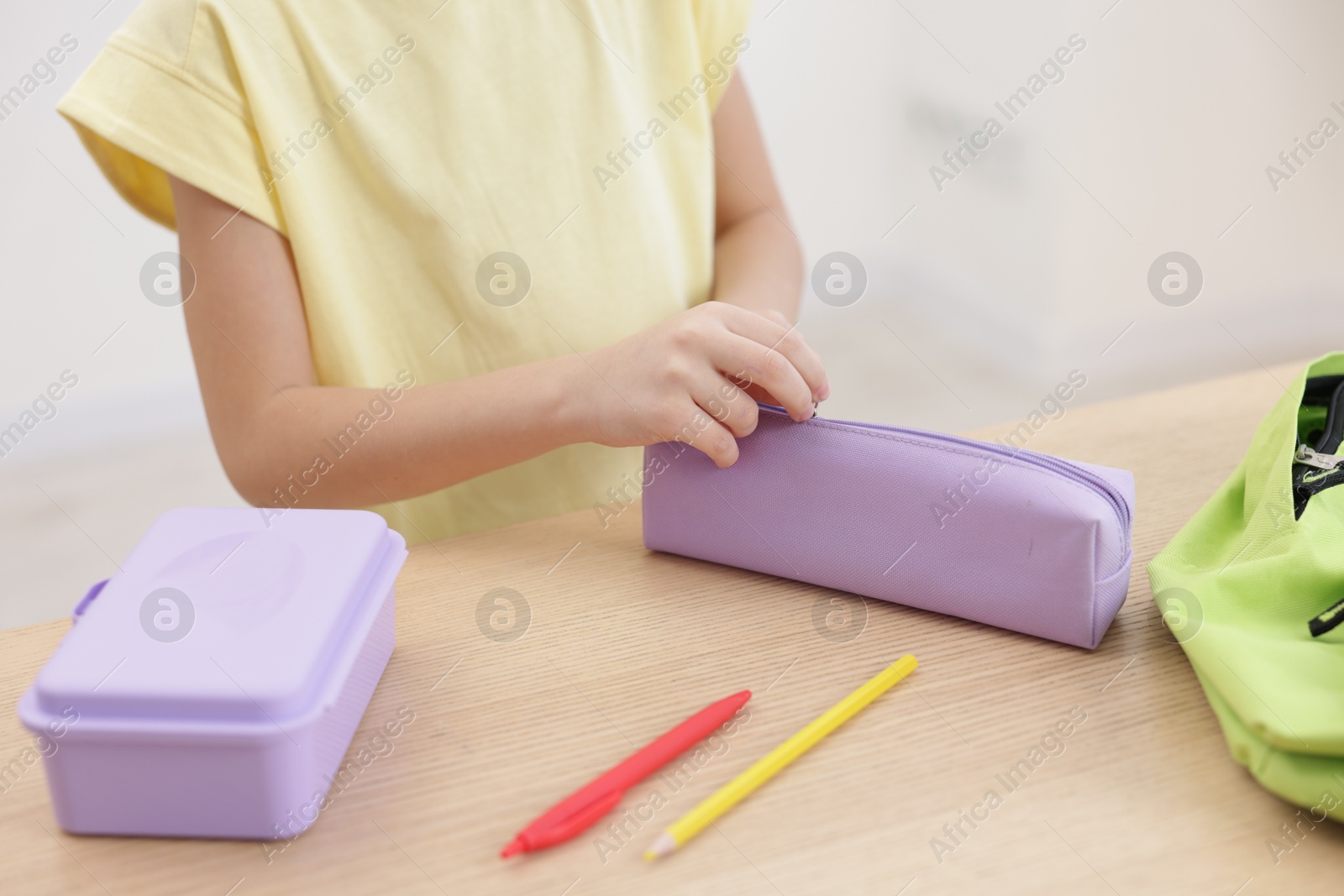 Photo of Little girl packing pencil case at wooden table indoors, closeup