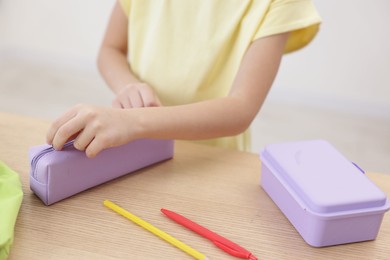 Little girl packing pencil case at wooden table indoors, closeup