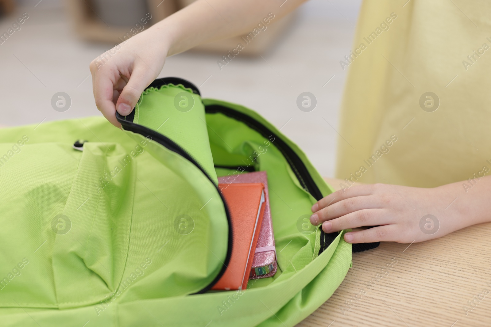 Photo of Little girl packing backpack at wooden table indoors, closeup