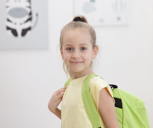 Little girl with backpack at home, space for text