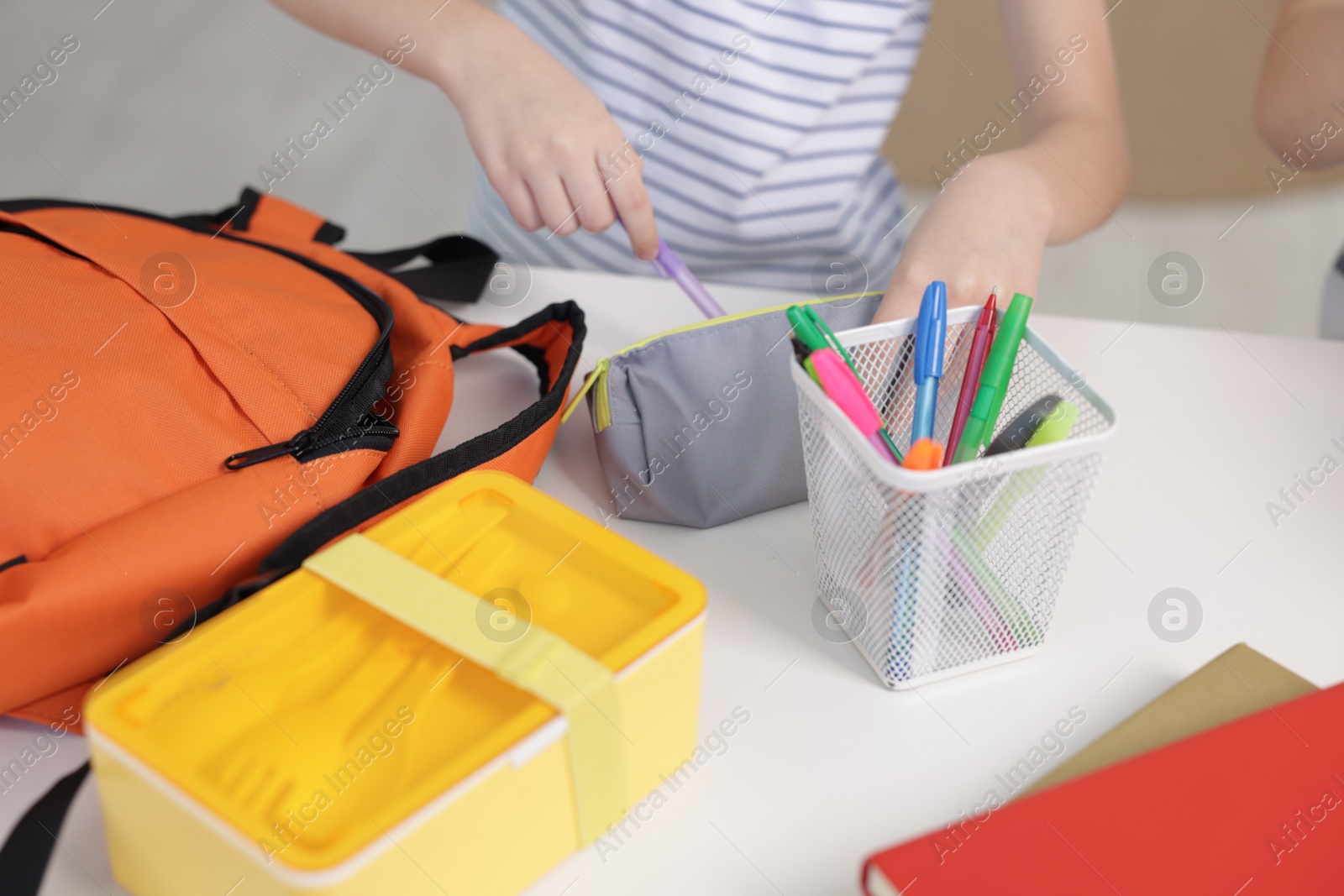 Photo of Little girl packing pencil case at table indoors, closeup