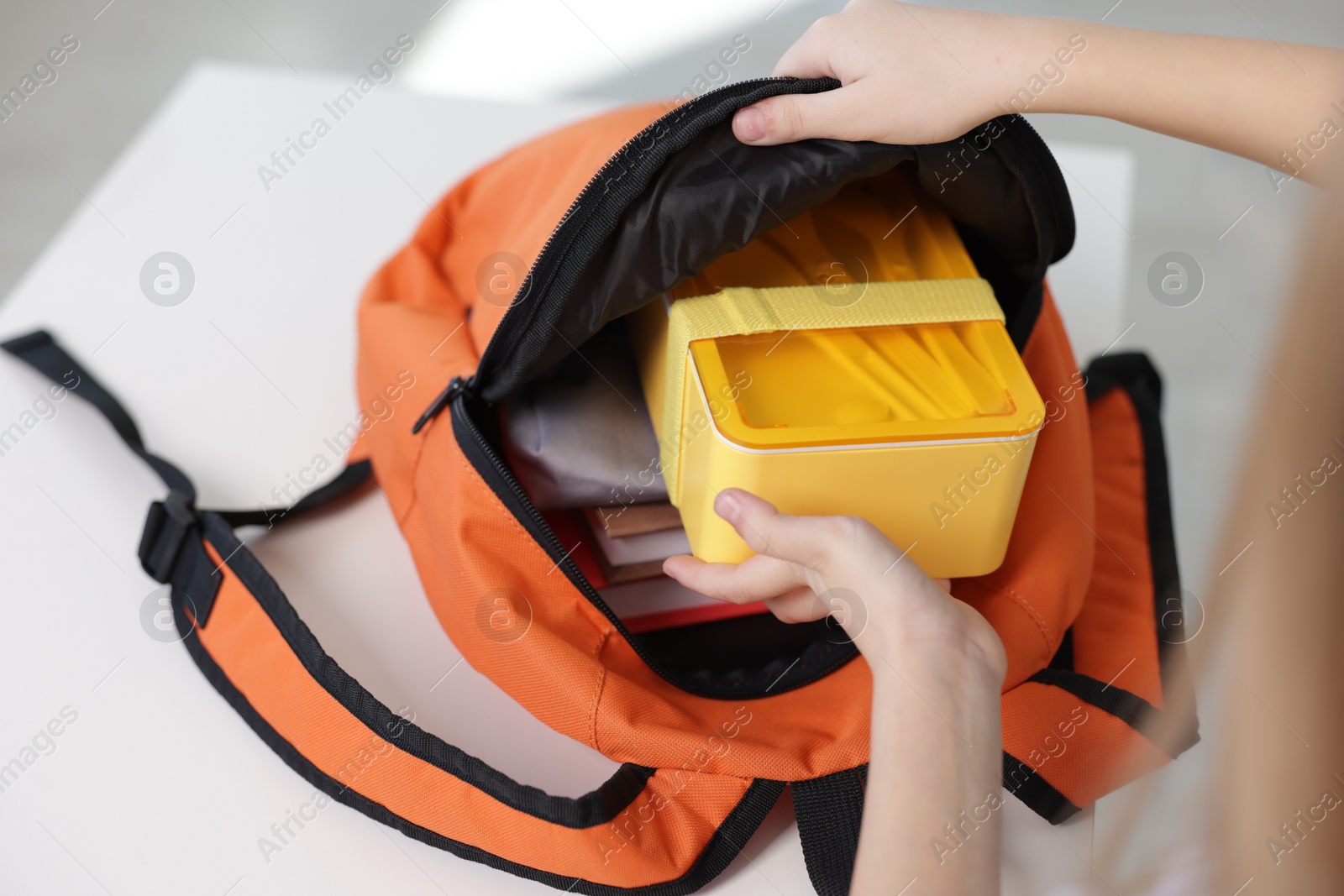 Photo of Girl packing lunch box into backpack at home, closeup