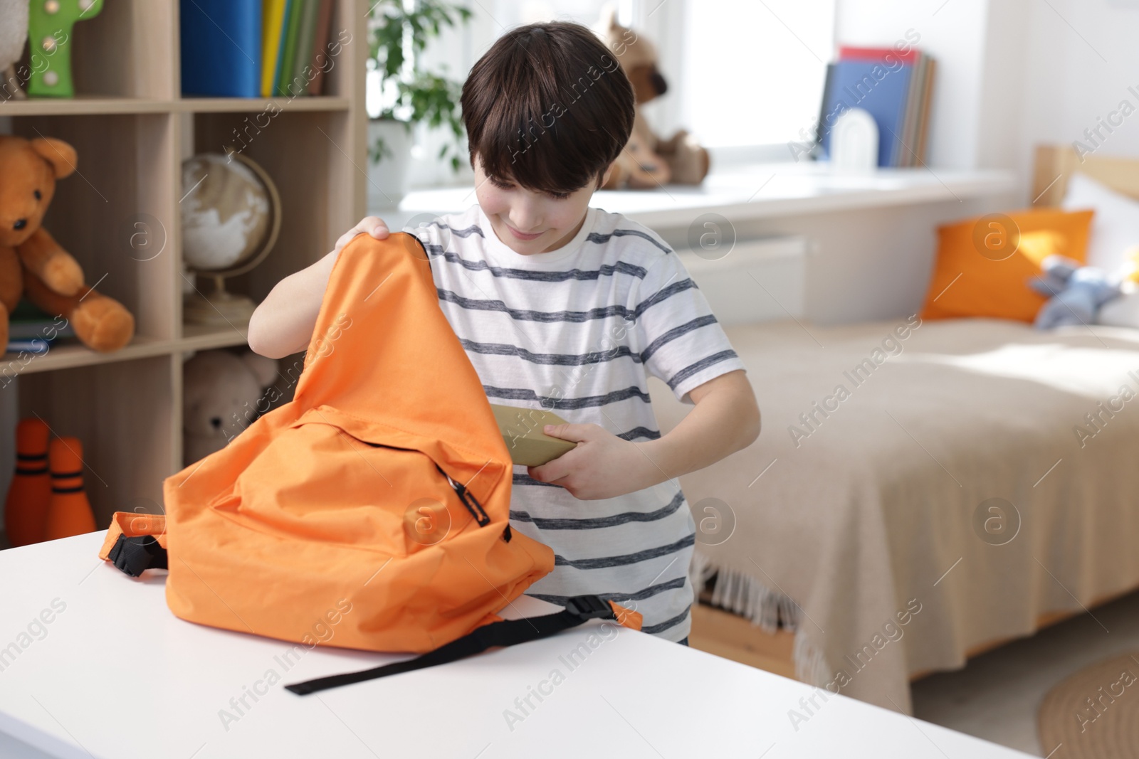 Photo of Boy packing backpack for school at table indoors