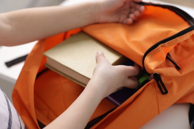 Photo of Boy packing backpack for school at home, closeup