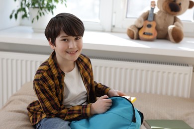 Boy packing backpack for school on bed at home