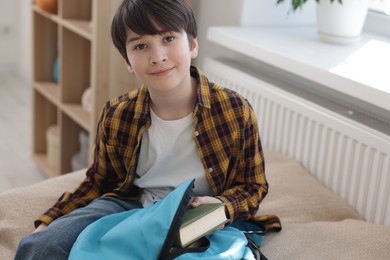 Boy packing backpack for school on bed at home