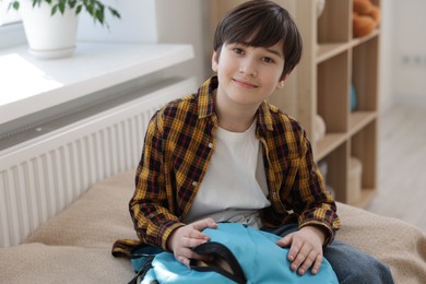 Boy packing backpack for school on bed at home