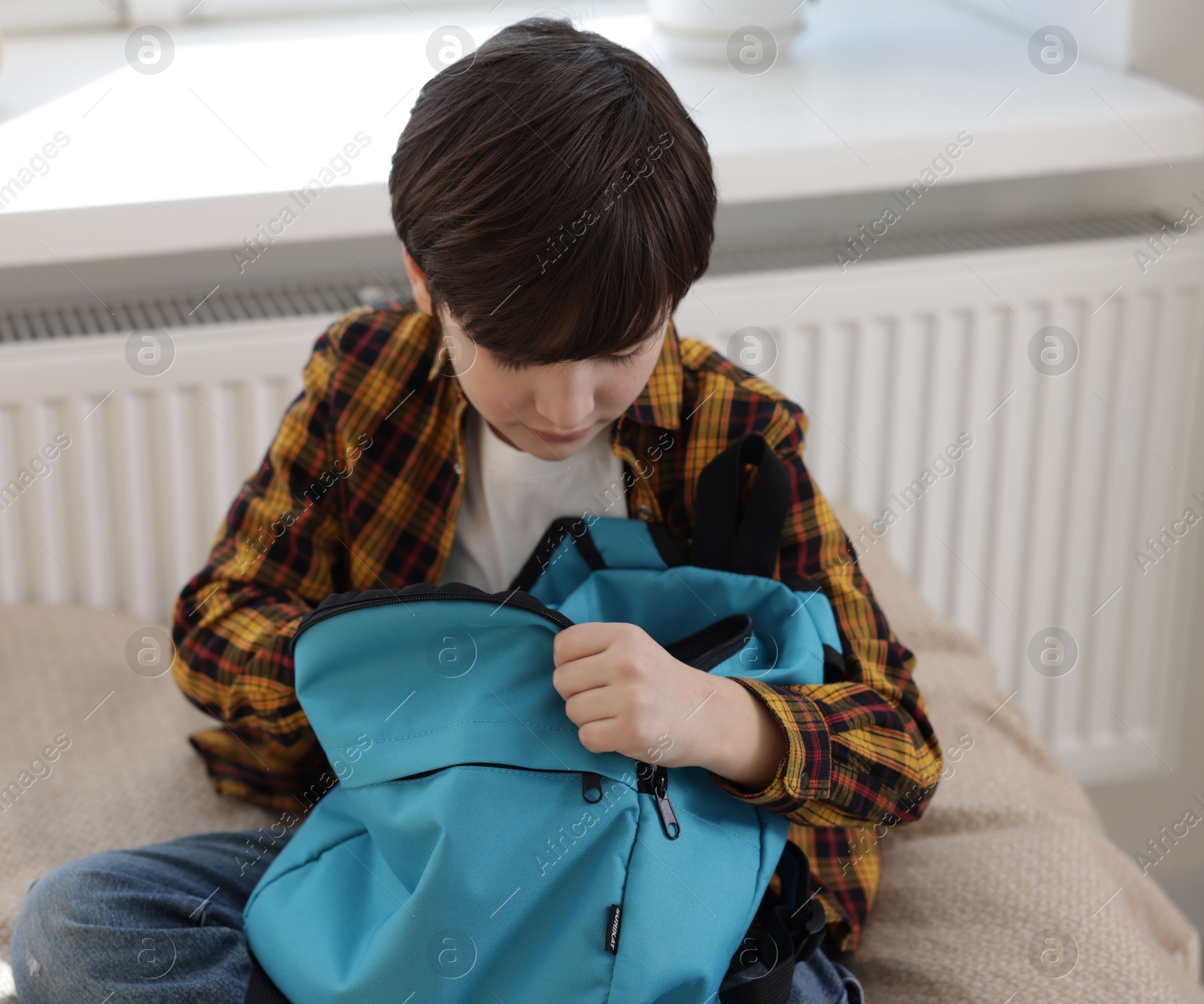 Photo of Boy packing backpack for school on bed at home